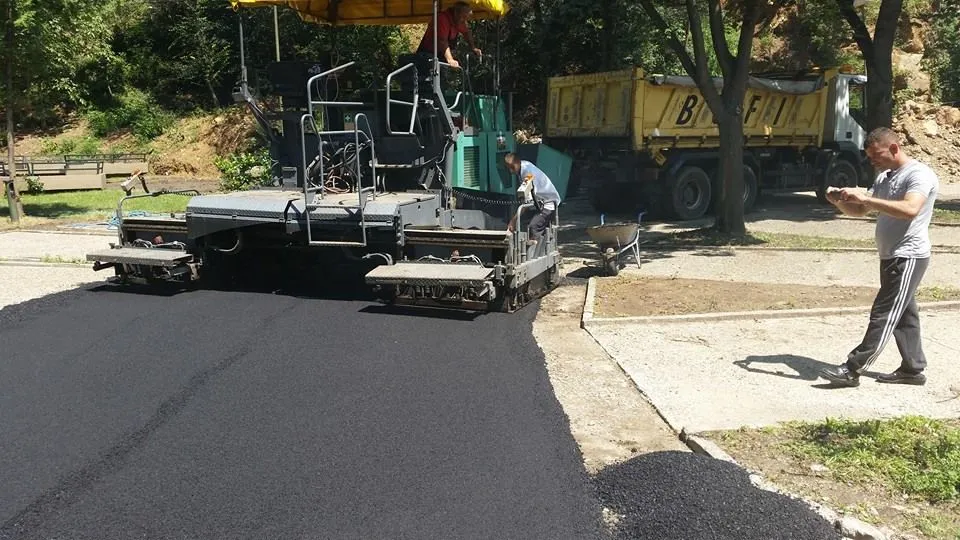 Finišer ugrađuje asfaltnu mešavinu dok radnik prati nivelaciju
