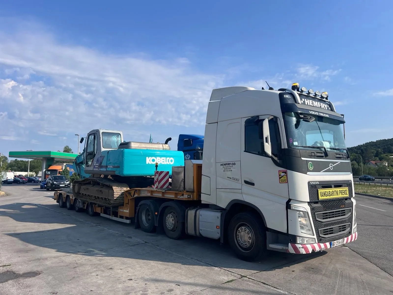 Bager Kobelco na niskonosećoj prikolici iza belog Volvo tegljača